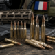 Cartouches de 5,56 et 7,62 mm devant un fusil et un drapeau français