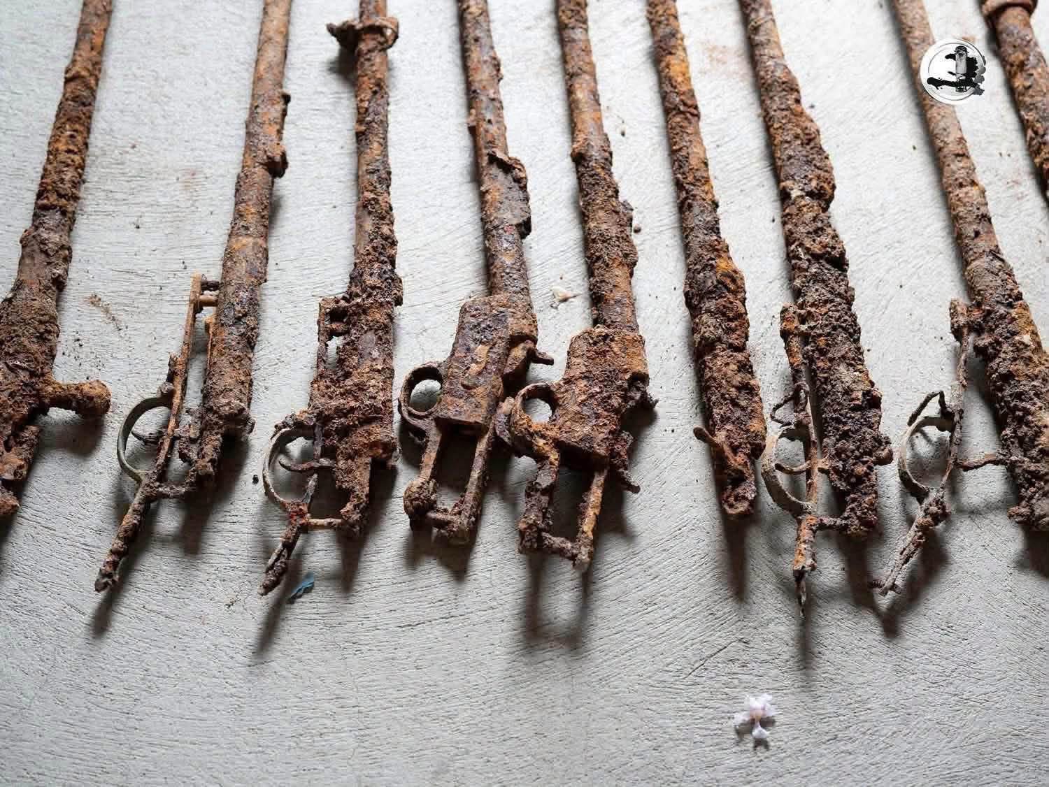 Rangée de fusils anciens corrodés, détail des platines et pontets