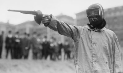 Duelliste masqué en sarrau de protection pointant un pistolet de duel, New York, vers 1909