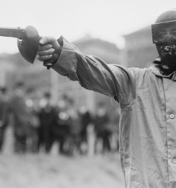 Duelliste masqué en sarrau de protection pointant un pistolet de duel, New York, vers 1909