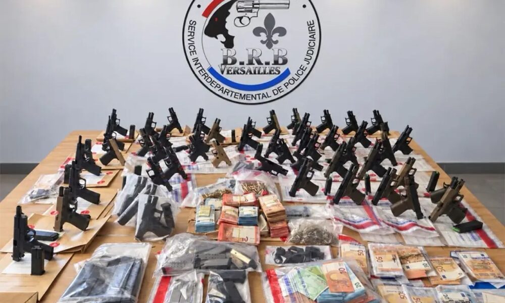 Dizaines de pistolets neufs, chargeurs et liasses de billets exposés sur une table devant l'écusson de la BRB de Versailles