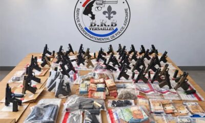Dizaines de pistolets neufs, chargeurs et liasses de billets exposés sur une table devant l'écusson de la BRB de Versailles