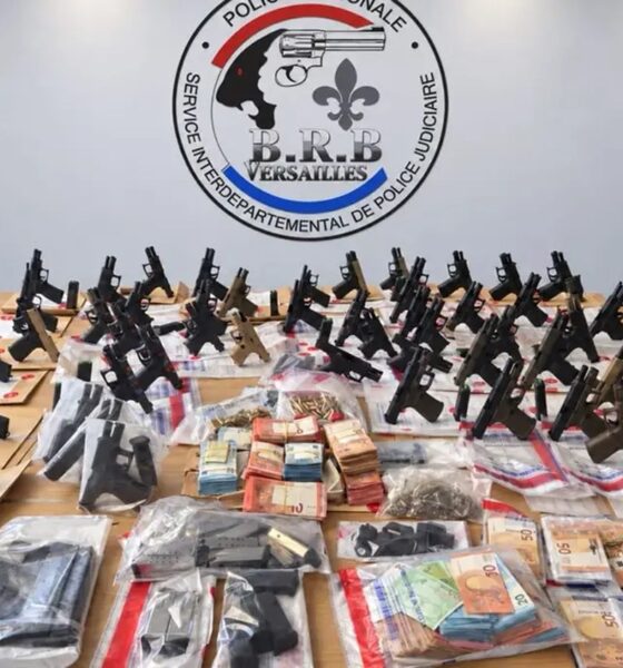 Dizaines de pistolets neufs, chargeurs et liasses de billets exposés sur une table devant l'écusson de la BRB de Versailles